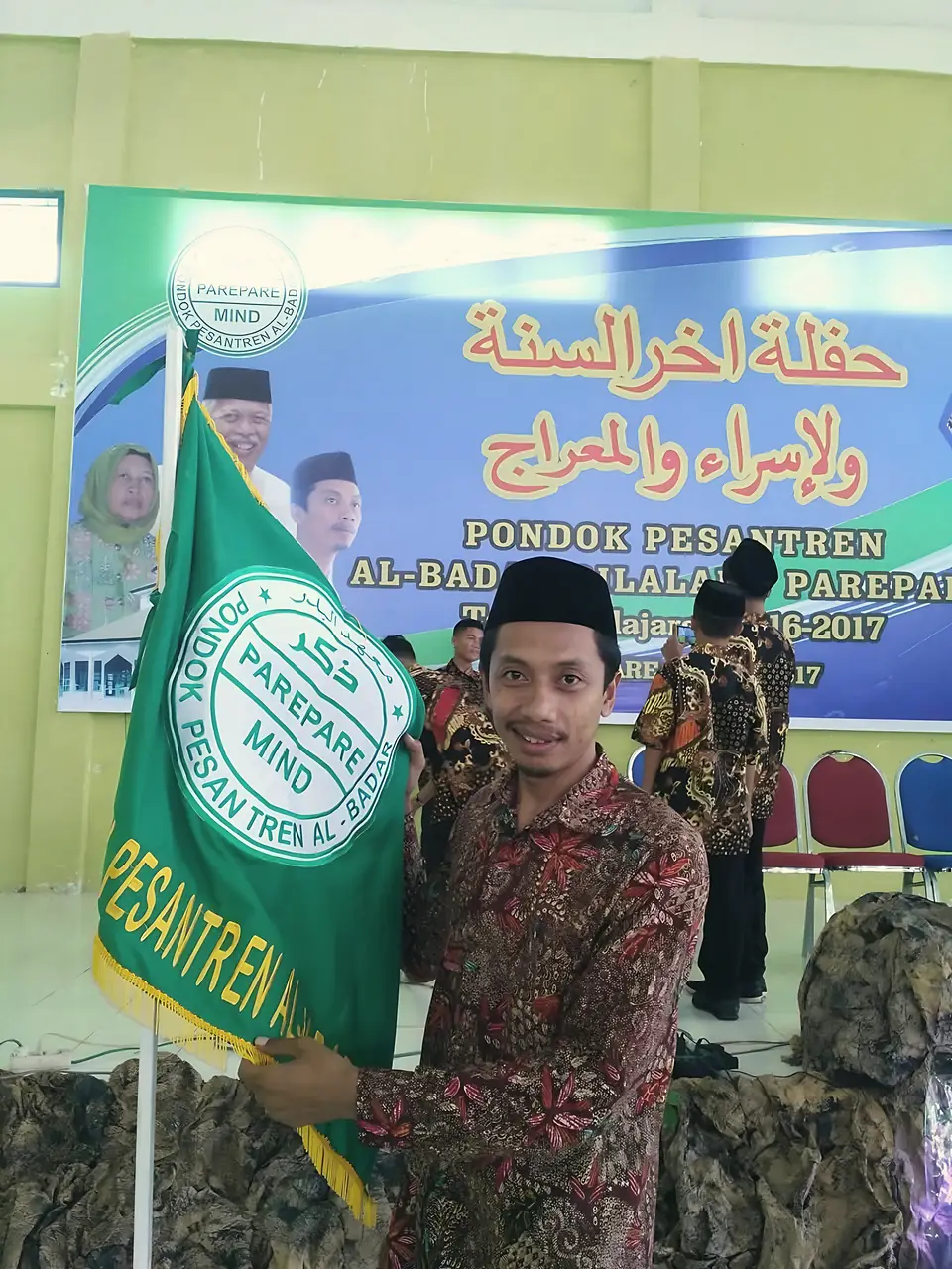 Seorang ustadz membentangkan bendera hijau Pondok Pesantren Al-Badar di depan spanduk Haflah Akhirus Sanah dan Isra Mi’raj