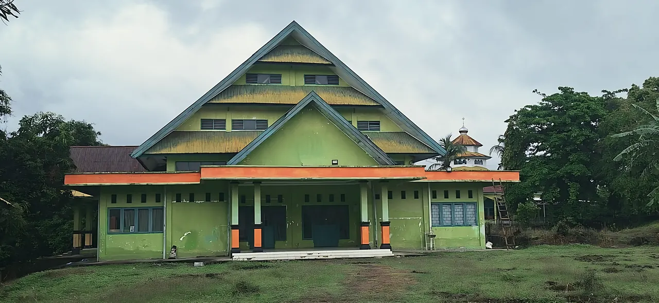 Gedung pesantren berwarna hijau dengan atap bertingkat di tengah halaman berumput