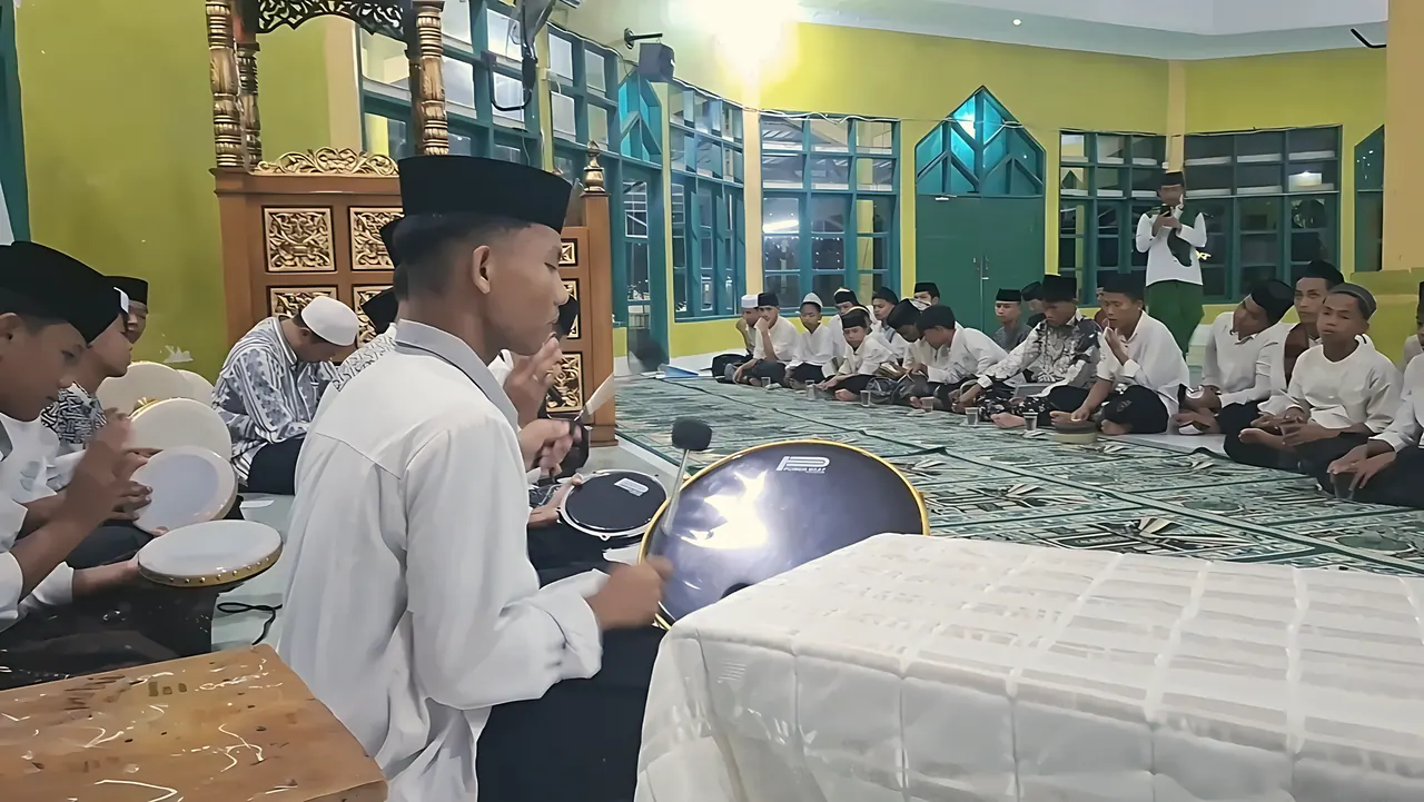 Santri memainkan rebana hadroh di masjid pada malam hari, disaksikan santri lain yang duduk berjajar